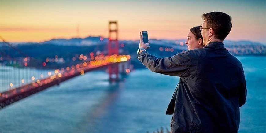 Mand og kvinde tager billede af Golden Gate Bridge ved solnedgang