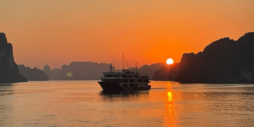 Skib badet i aftensol ved solnedgang i Halong Bay